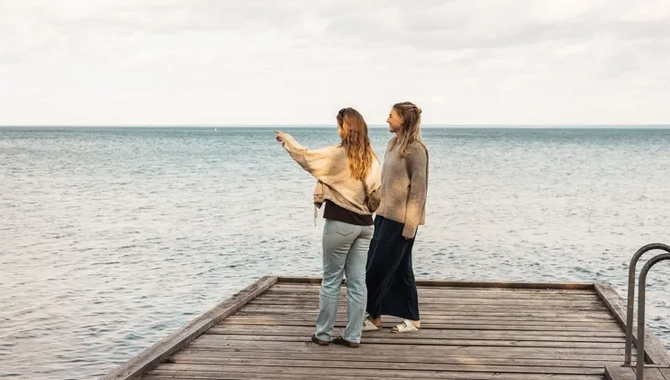Två kvinnor står på en brygga och pekar på vattnet.