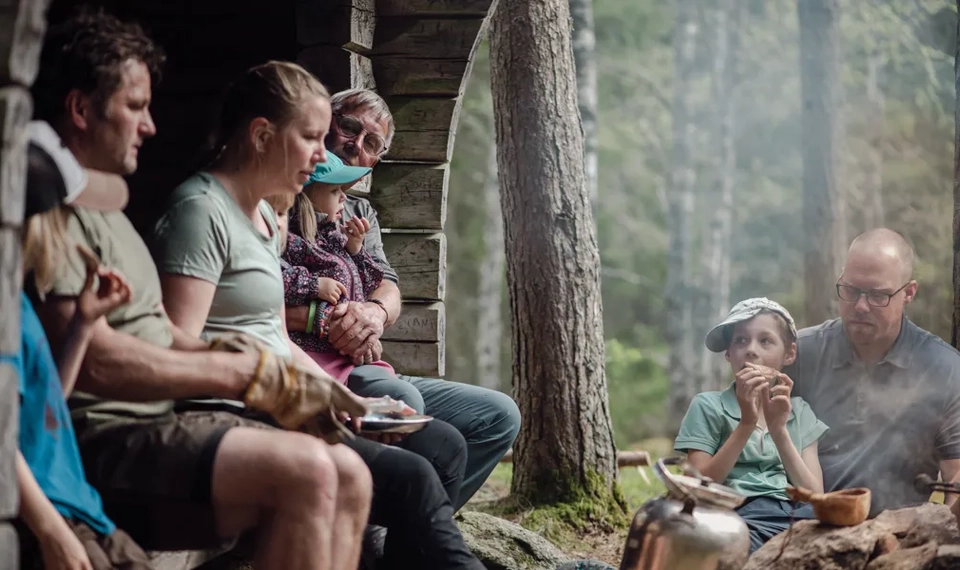 Vuxna och barn som sitter i och vid ett vindskydd och fikar.