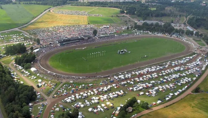 En flygbild av en travbana med många bilar och husvagnar parkerade runt den.