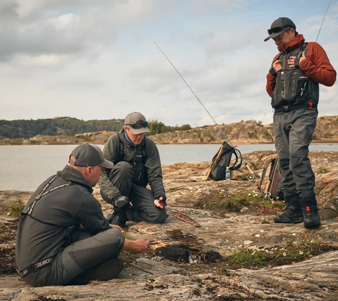 En grupp män som sitter på en klippa intill ett vattendrag.
