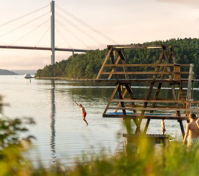 Badgäster hoppar från hopptorn med Tjörnbron i bakgrunden vid Lilla Brattön
