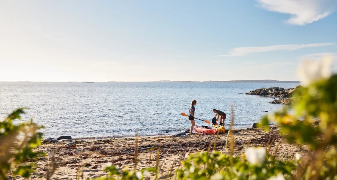 Två kvinnor drar upp sina kajaker på en strand.