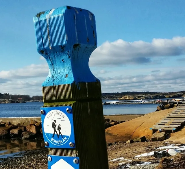 En blåvit skylt på en trästolpe intill havet.