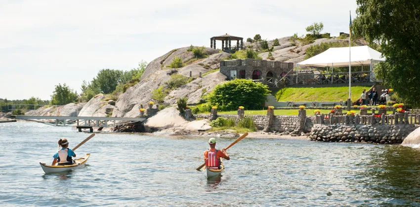 Två personer i kajak paddlar mot sten- och blomsterträdgården Alaska.