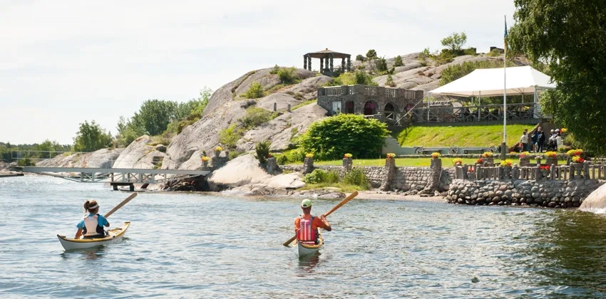Två personer i kajak paddlar mot sten- och blomsterträdgården Alaska.