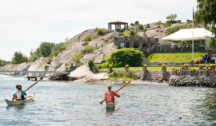 Två personer i kajak paddlar mot sten- och blomsterträdgården Alaska.