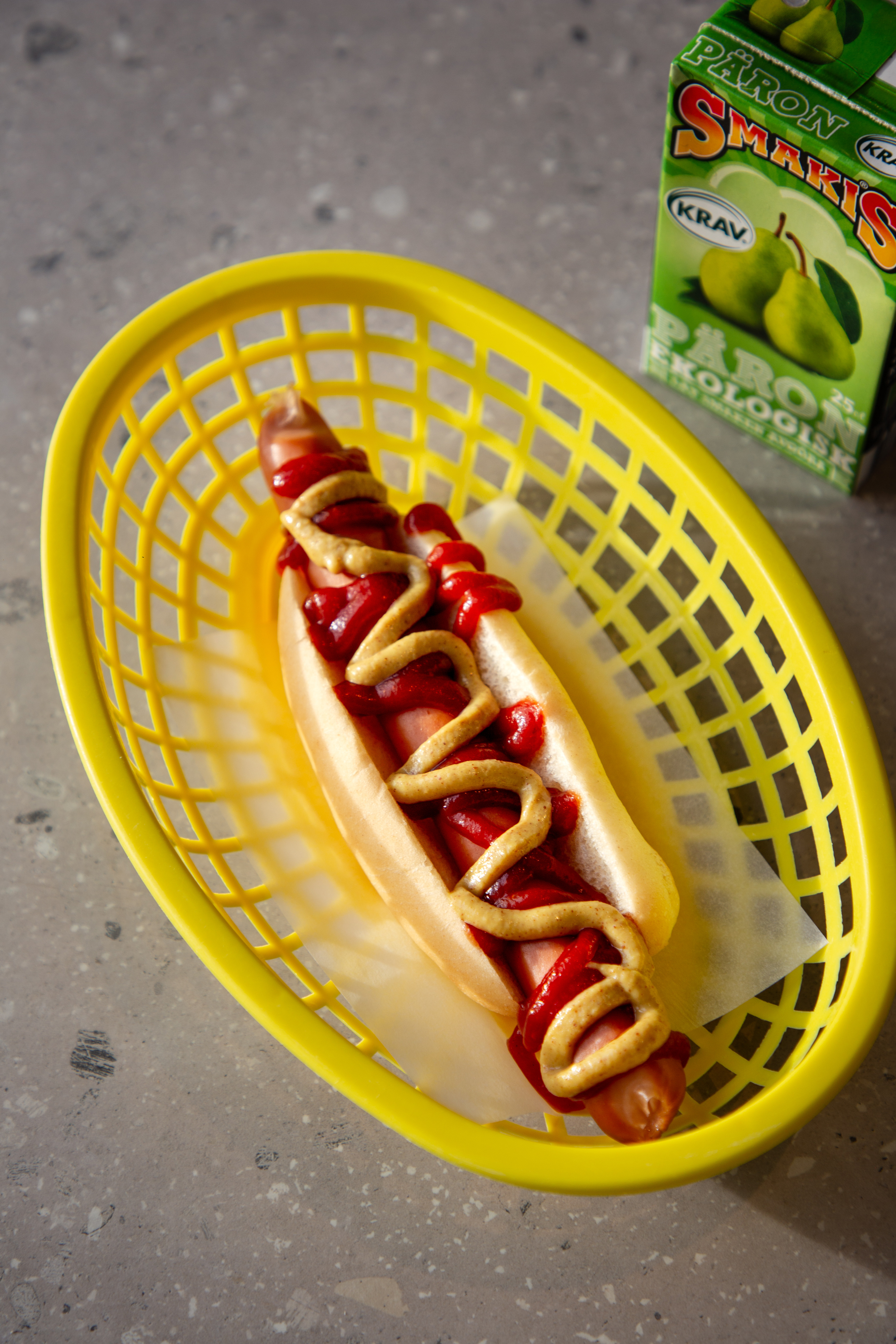 En varmkorv med ketchup och senap i en gul korg.