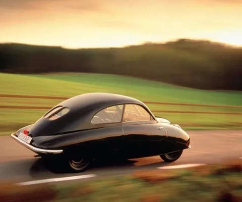 En svart bil kör längs en väg bredvid ett grönskande fält.