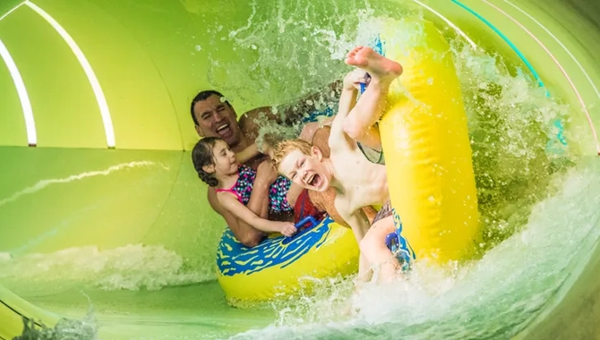 En man, en flicka och en pojke sitter i stora badringar och åker ned i full fart i en vattenrutschbana