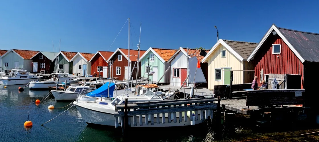 En massa båtar ligger vid kaj vid färgglada sjöbodar