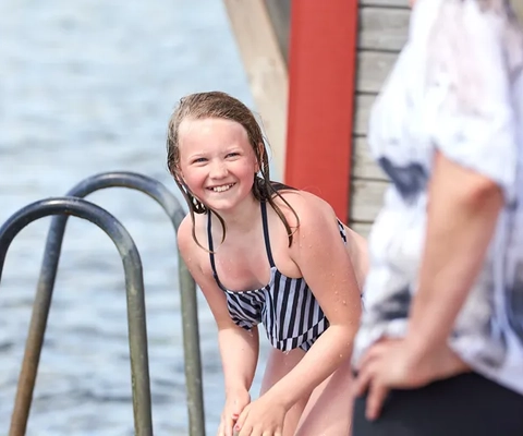 Ett barn i svarvit randig baddräkt står bredvid en kvinna.