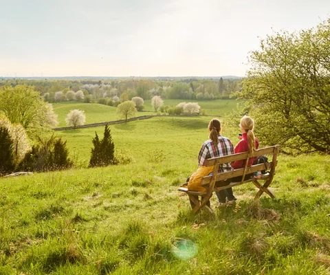 Två personer sitter på en bänk på ett fält.
