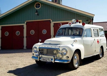 En vit ambulans parkerad framför en grön byggnad.