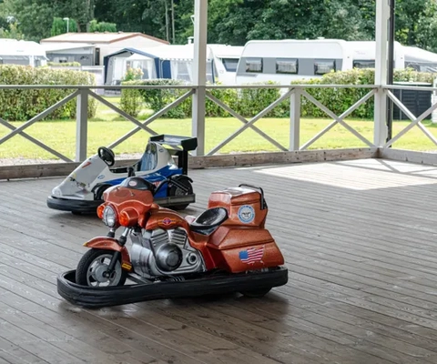 Två elbilar till barn på en camping, bilarna står på ett trädäxk med ett tak under