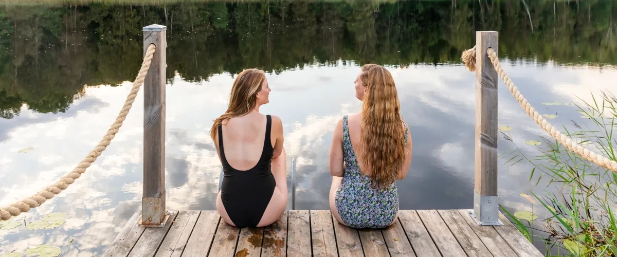 Två kvinnor sitter på en brygga vid en sjö.