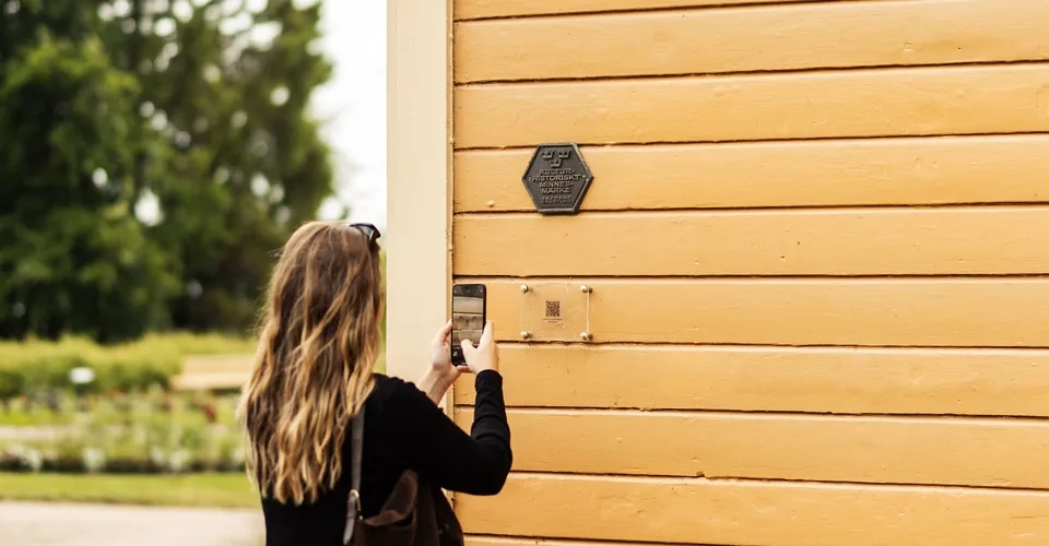 Kvinna står och skannar en qr-kodsskylt på ett hus