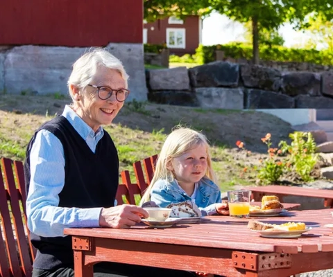Ett sällskap fikar utomhus sittande vid ett bord.