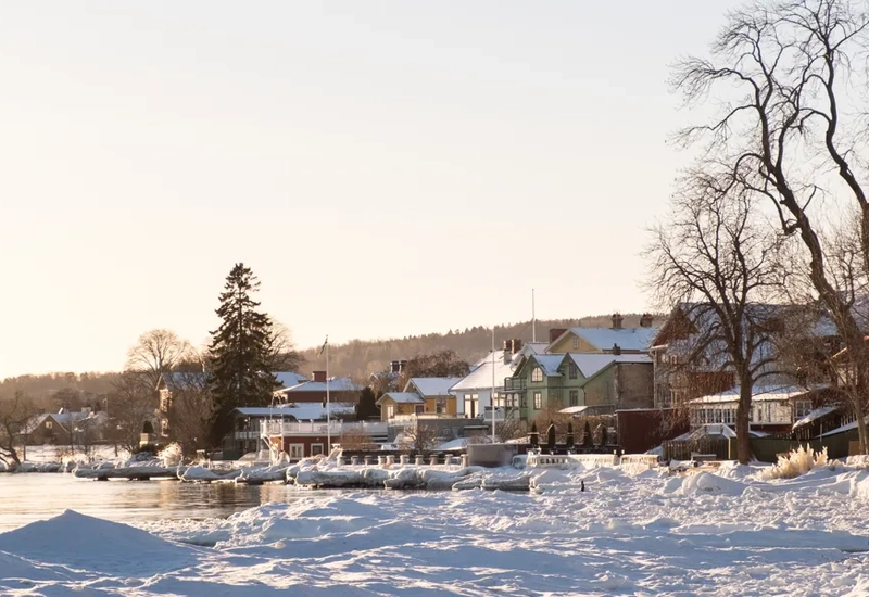 Bild över trähus längs en sjö med snö runt omkring