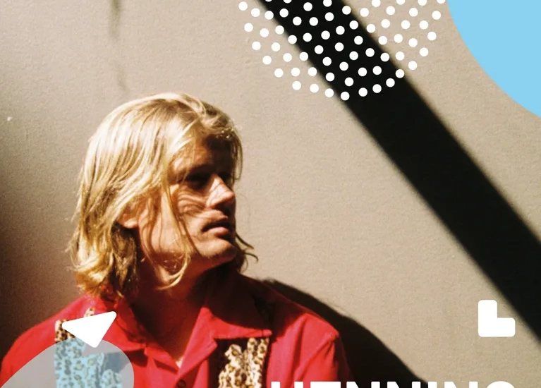 En man i röd skjorta står framför en vägg.