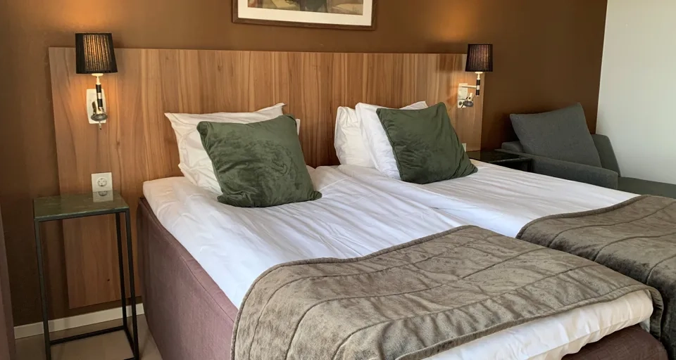 en dubbelsäng med bruna filtar på och en brun vägg bakom.