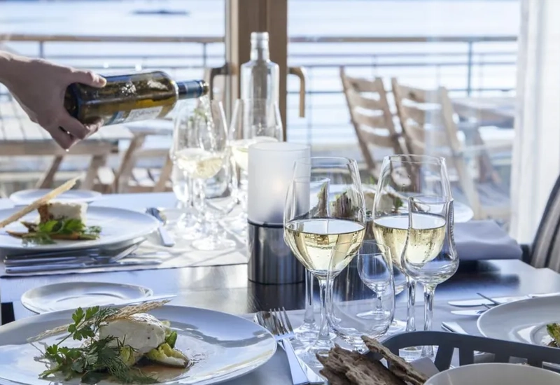 En person som häller upp en flaska vin vid ett bord med tallrikar med mat och glas med vin.