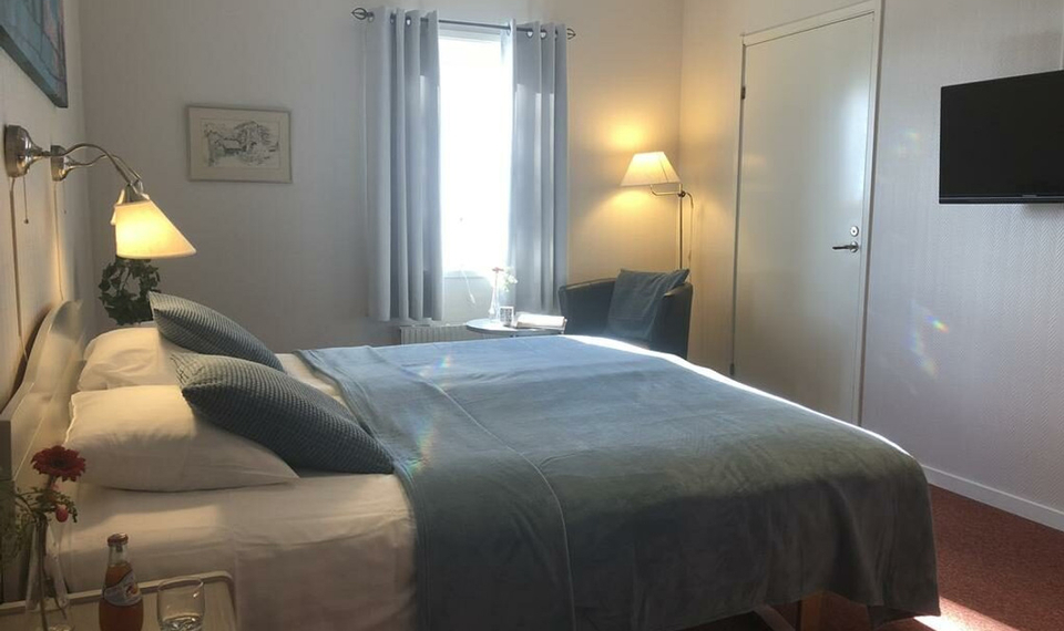 Ljust rum med en dubbelsäng som har grå/blått överkast.