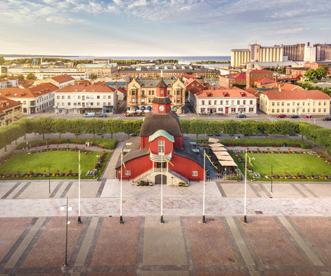 Rådhuset- en röd träbyggnad med fyra våningar. Bilden är tagen något uppifrån vilket gör att det går att skymta sjön Vänern i bakgrunden. i bakgrunden syns även flertal hus och byggnader.