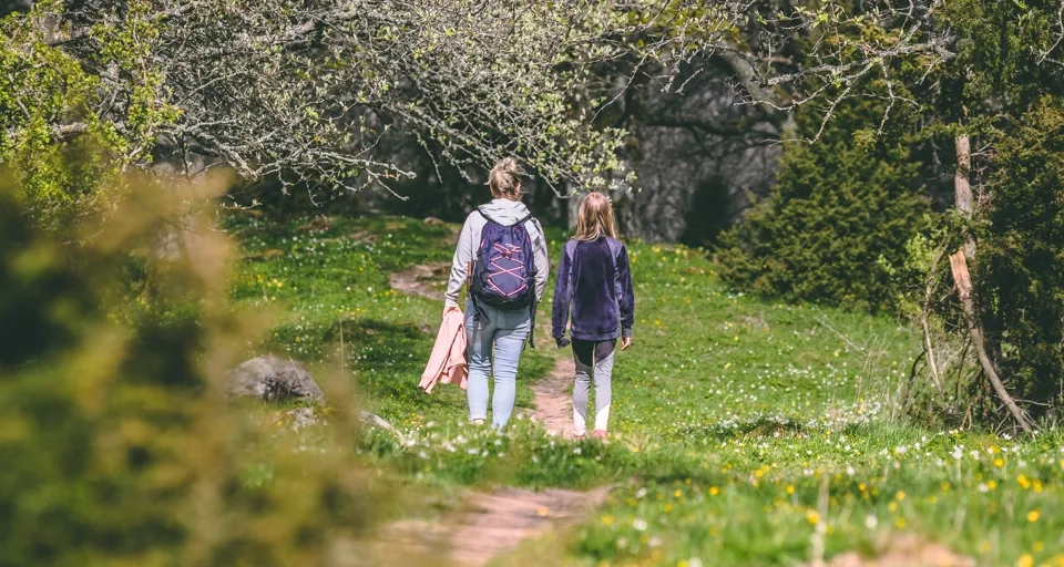 En kvinna och ett barn promenerar längs en stig i en skog med blommor på marken.