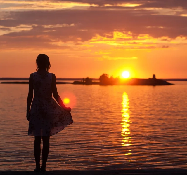 En kvinna står på en strand och tittar på solnedgången.