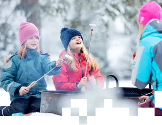 En familj i färgglada vinterkläder sitter i vinterlandskapet på Billingen i Skövde och grillar korv.