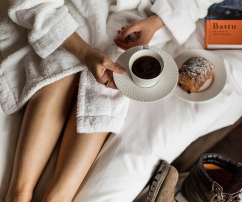 A woman sitting on a bed holding a cup of coffee.