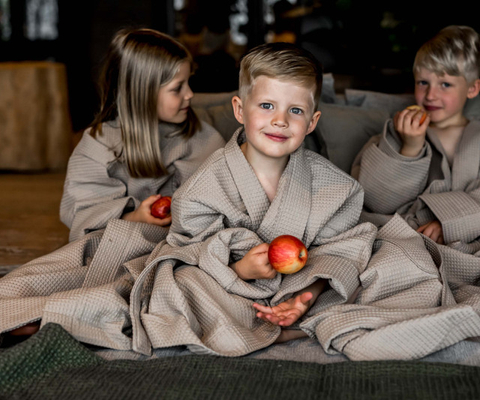Tre barn sitter med morgonrock på sig och med äpple i handen. 