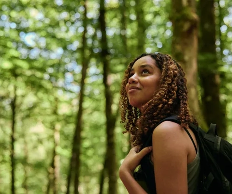 En kvinna som står i skogen med en ryggsäck.