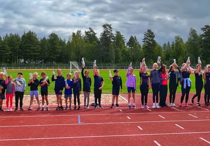 En grupp med barn i olika åldrar som står på en idrottsplats. 