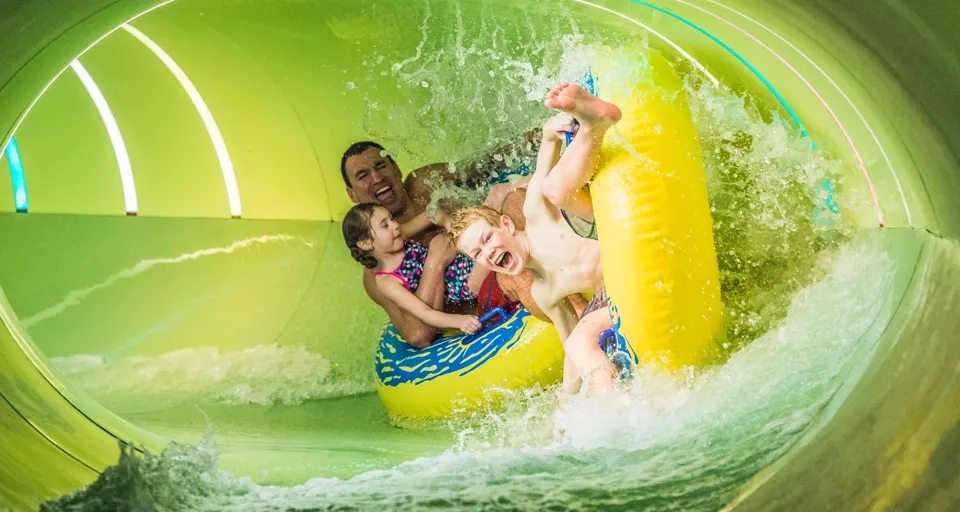 Två barn och en man åker tillsammans på badringar i en vattenrutschkana.