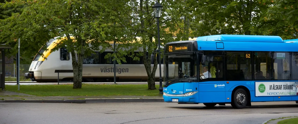 En blå buss som kör längs en gata bredvid ett tåg.