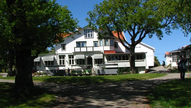 Hotel Koster Ekenäs, vit träbyggnad med grönvita markiser och högväxta ekar framför hotellet.