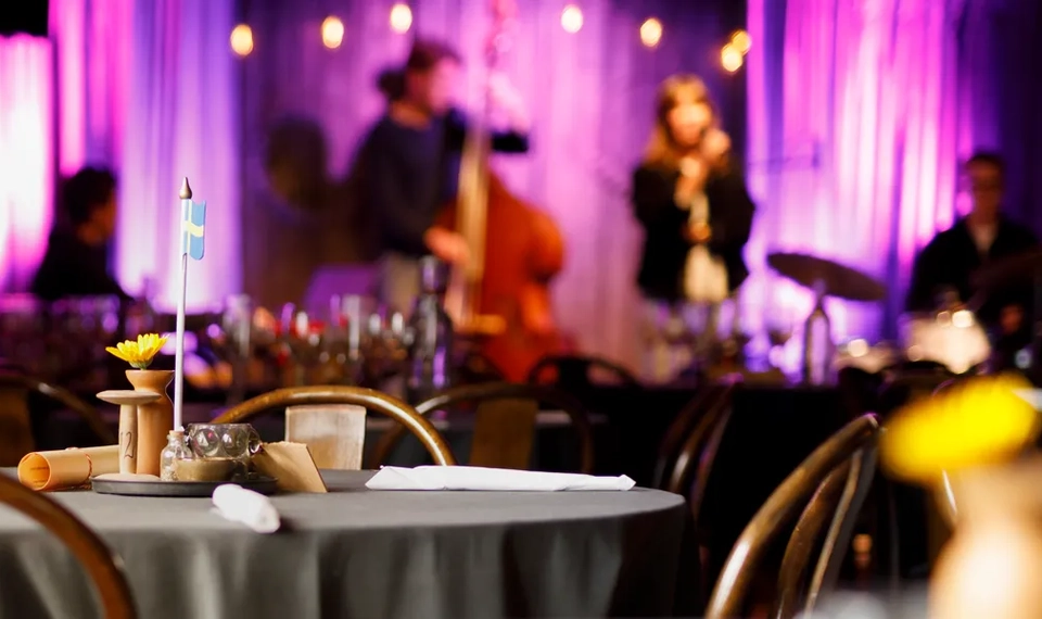 Musiklokal med scen och dukade bord.