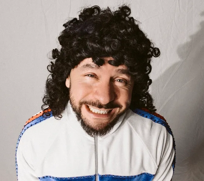 En man med lockigt hår och skägg ler.