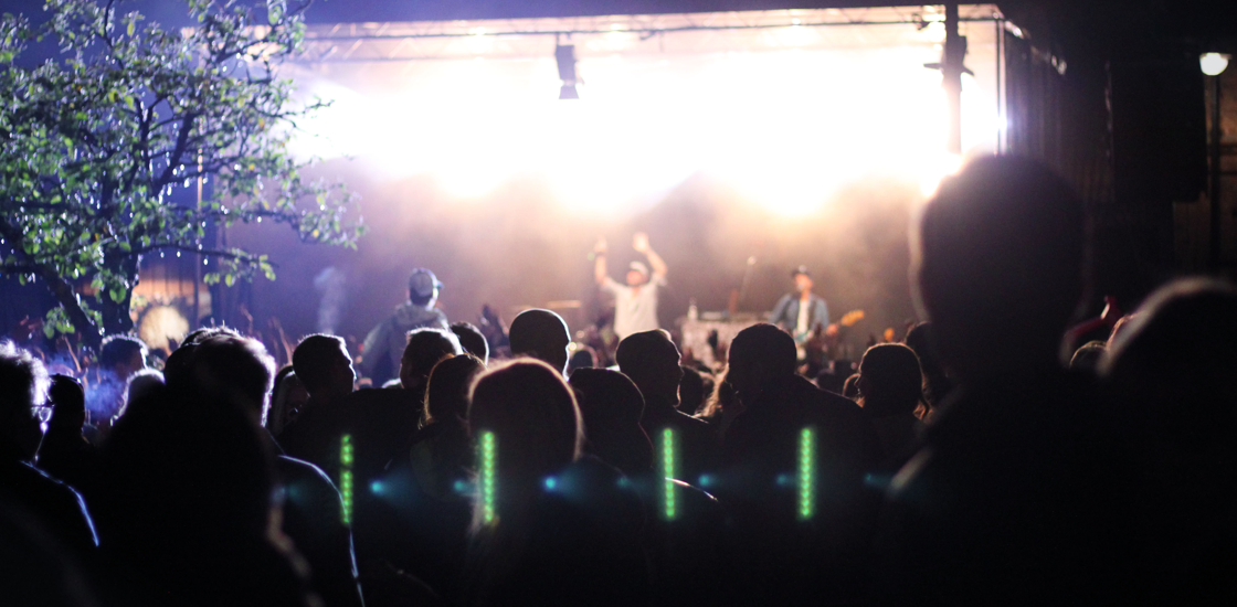 En artist uppträder på en upplyst scen på kvällen. Publiken syns som skuggor framför scenen.