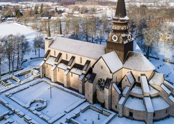 Drönarbild över Varnhems klosterkyrka med snö på taket och det omkringliggande landskapet.