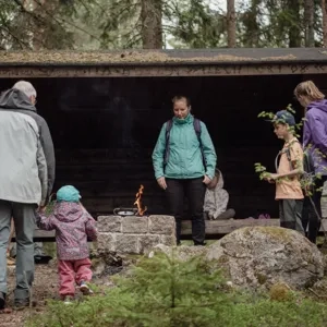 Flera personer som står vid ett vindskydd i skogen.