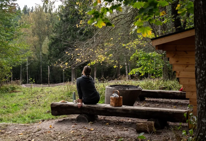 En person sitter vid ett vindskydd i skogen