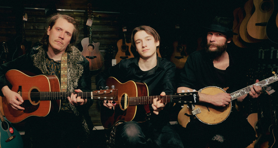 En grupp män som sitter runt varandra och håller i gitarrer.