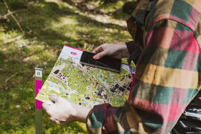 En person håller i en orienteringskarta och en mobil i handen
