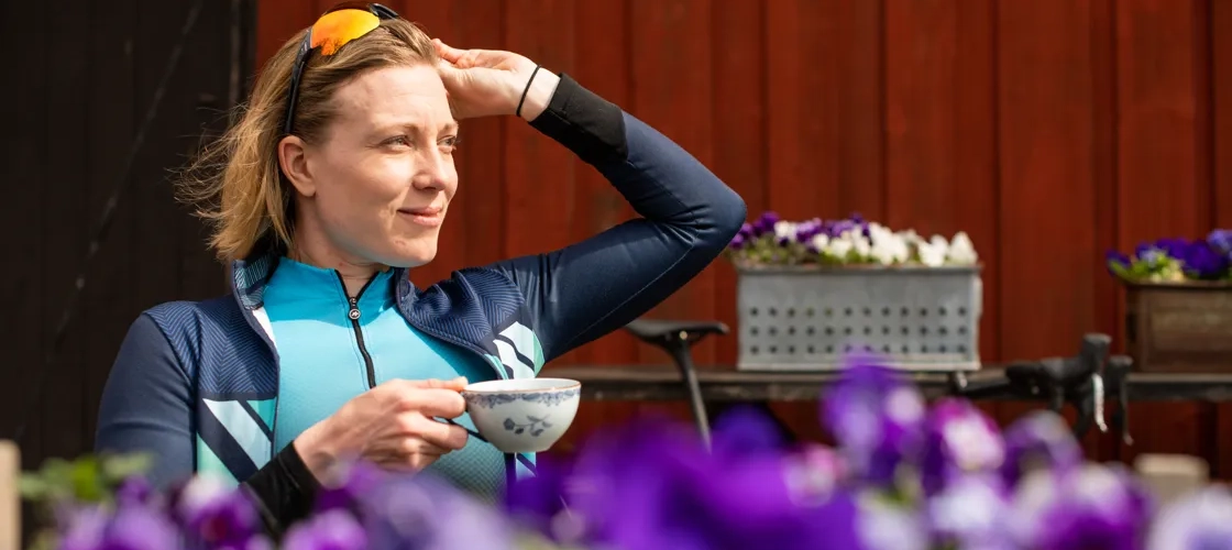 En kvinna som håller i en kaffekopp framför lila blommor.