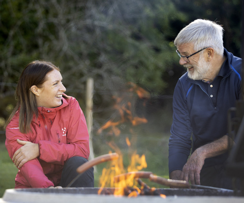 Younger woman and older man sitting and grilling sausages.