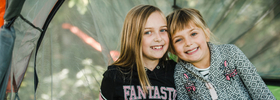 Två unga flickor står bredvid varandra framför ett tält.