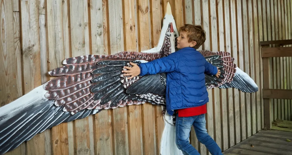 En ung pojke står bredvid en stor fågelskulptur.