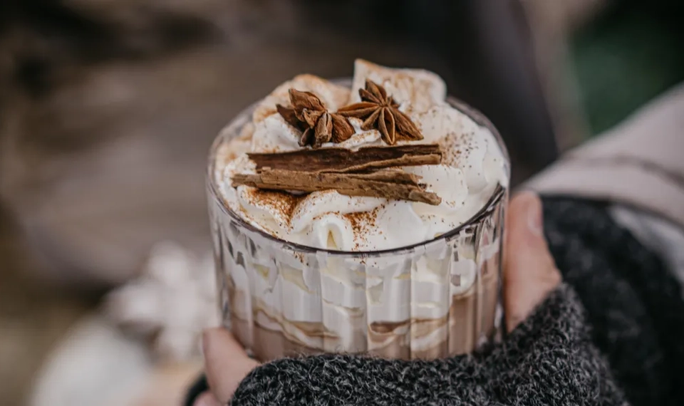 En person som håller i en kopp kaffe med kanel på toppen.